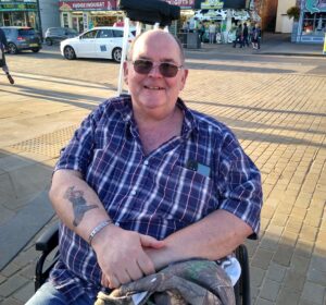 Andrew smiling sat in his wheelchair outside in the shade